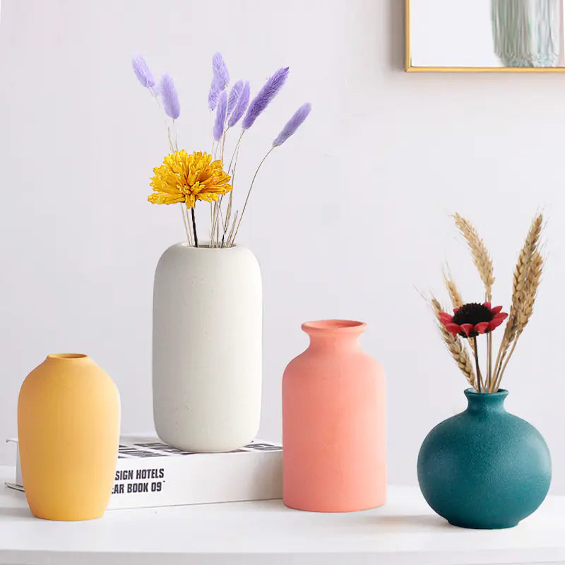 Four colorful vases with dried flowers on a white surface.