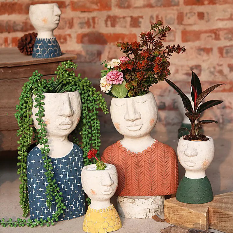 Decorative planters shaped like faces with plants inside, set against a brick wall.