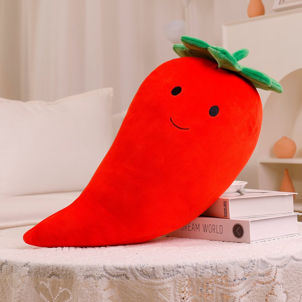 Red plush pepper toy with a smiling face on a surface with books in the background