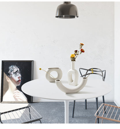 Modern interior with a round white table, decorative vase, and abstract art on a white wall.