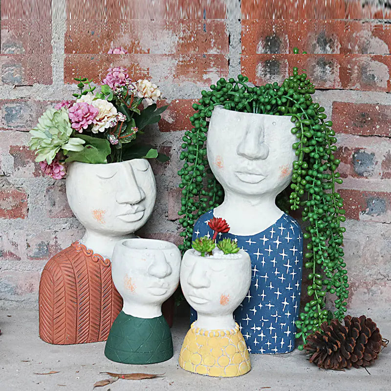 Set of face-shaped planters with plants against a brick wall.